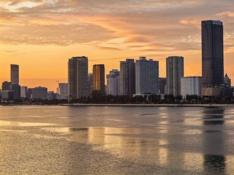 Urban skyline silhouetted against golden sunset sky reflected in calm waterfront.
