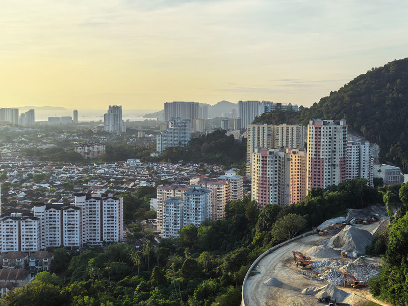 Aerial cityscape at golden hour with residential high-rises nestled among forested hills and distant urban sprawl.