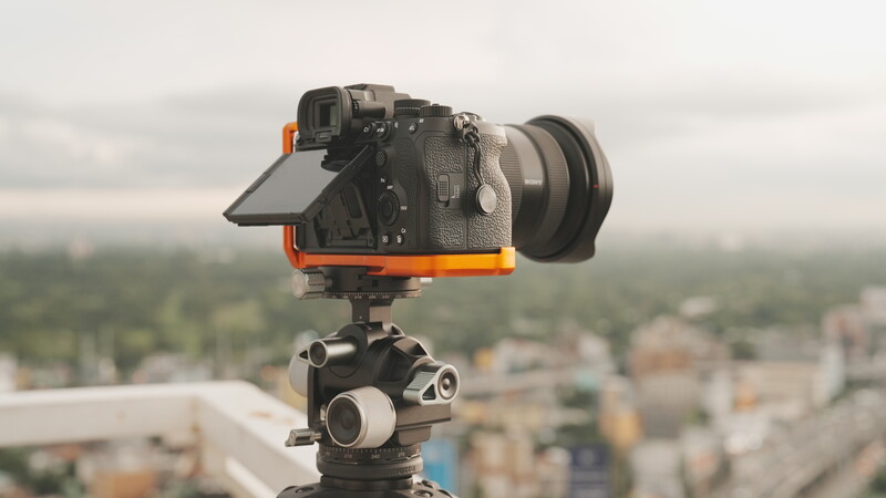 Professional cinema camera with orange support frame mounted on tripod head overlooking urban landscape.