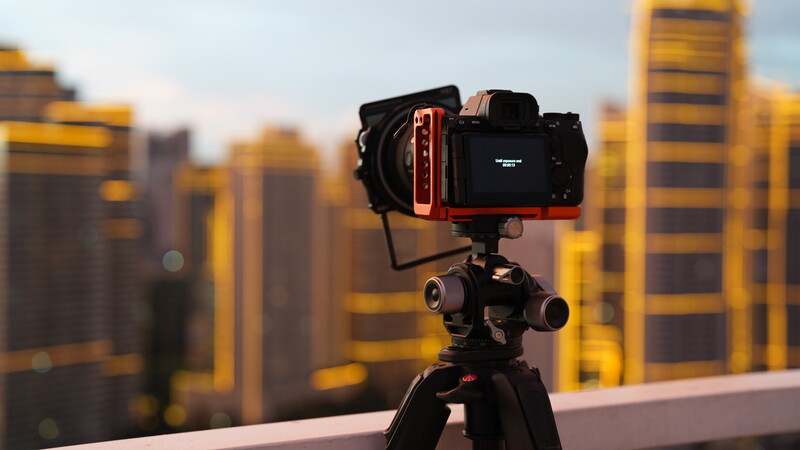 Professional mirrorless camera mounted on tripod overlooking cityscape during golden hour.