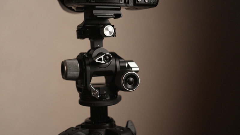 Professional gimbal head with dual camera mounting system mounted on tripod against neutral backdrop.