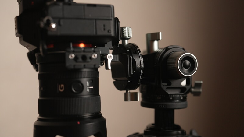 Cinema camera with telephoto lens mounted on gimbal stabilizer against neutral background.