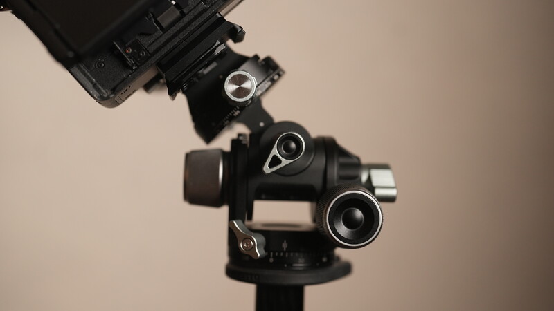 Professional gimbal head with multiple lens attachments mounted on a tripod against a neutral background.
