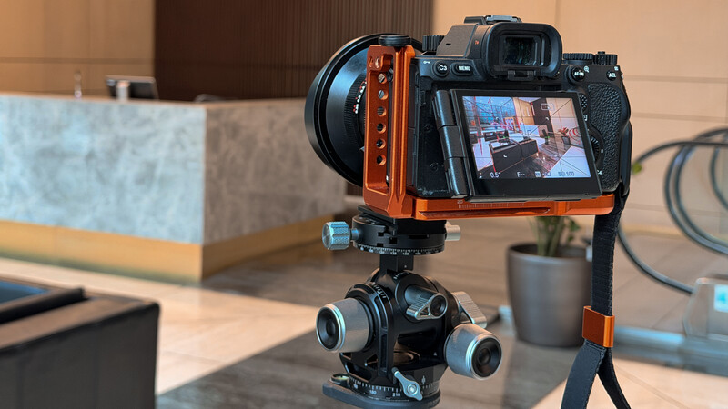 Mirrorless camera with orange cage rig mounted on gimbal head with blue counterweights.