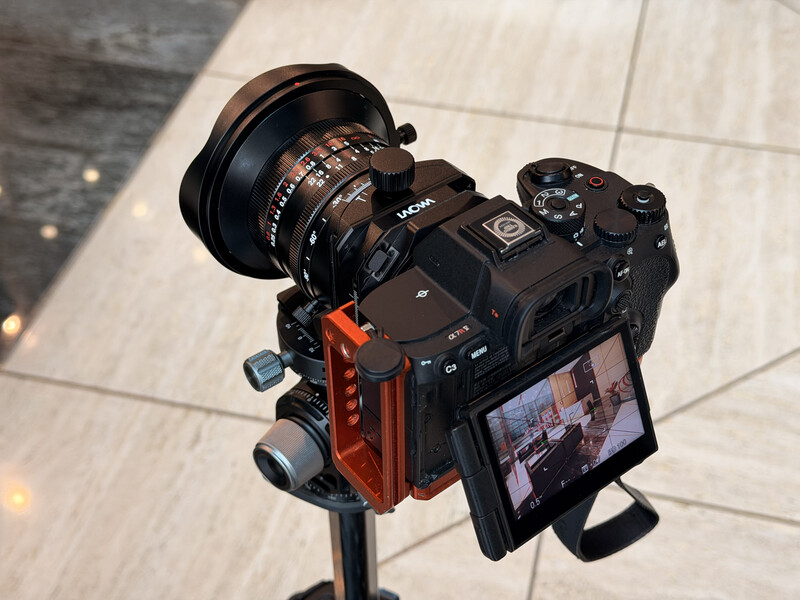 Cinema camera mounted on tripod with wide-angle lens and articulating monitor against tiled ground.