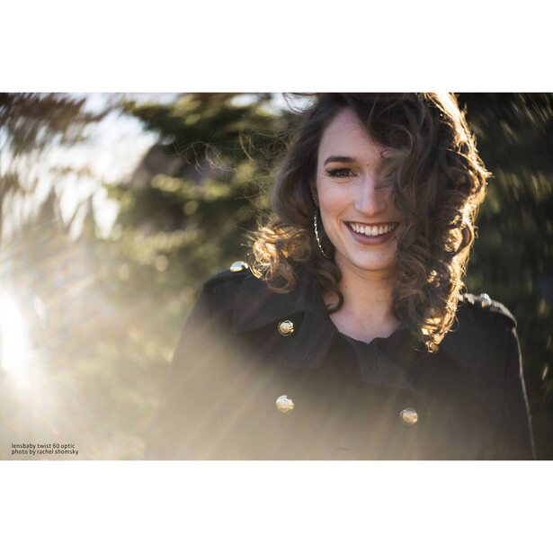 Woman with wavy dark hair smiling in golden hour sunlight with bokeh background.