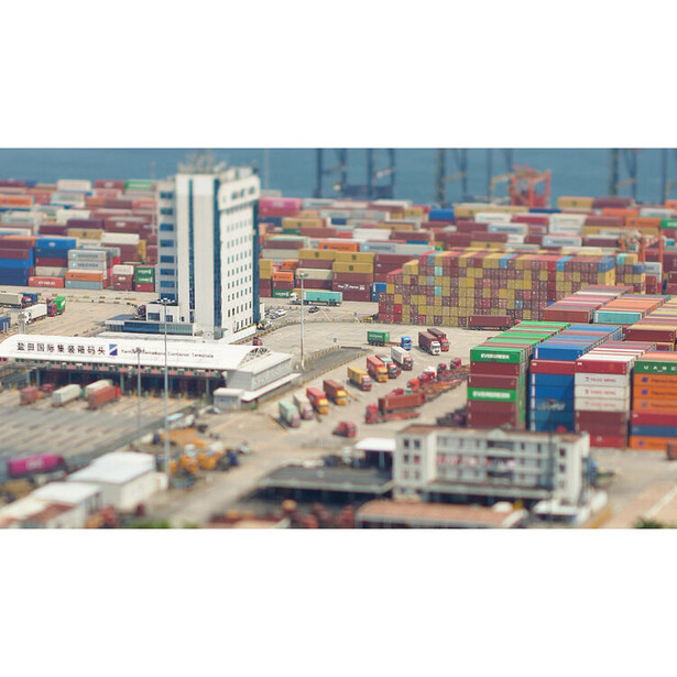 Aerial view of a busy shipping port with stacked cargo containers and a white warehouse building.
