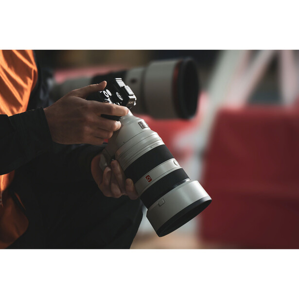 Photographer holding a telephoto zoom lens with white barrel and multiple focus rings.