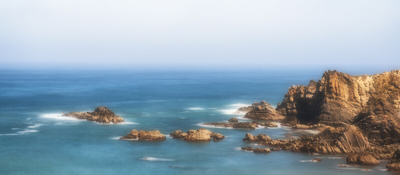 Midday blue bird sky over looking a seascape of rocks and water