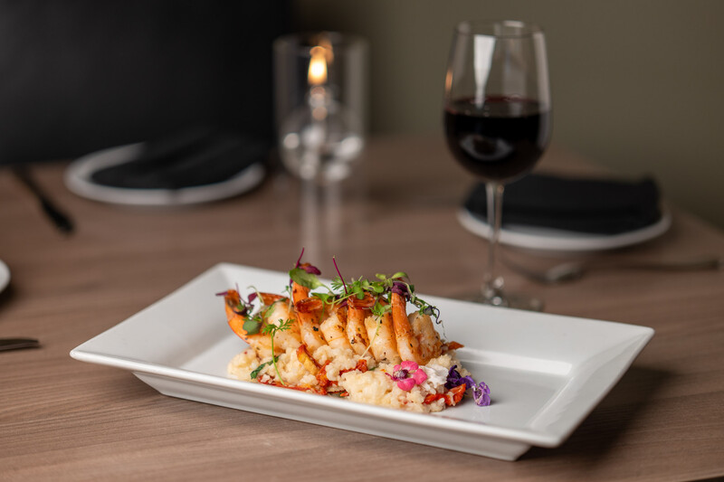 Plated shrimp dish with colorful vegetables on white rectangular plate at place setting.