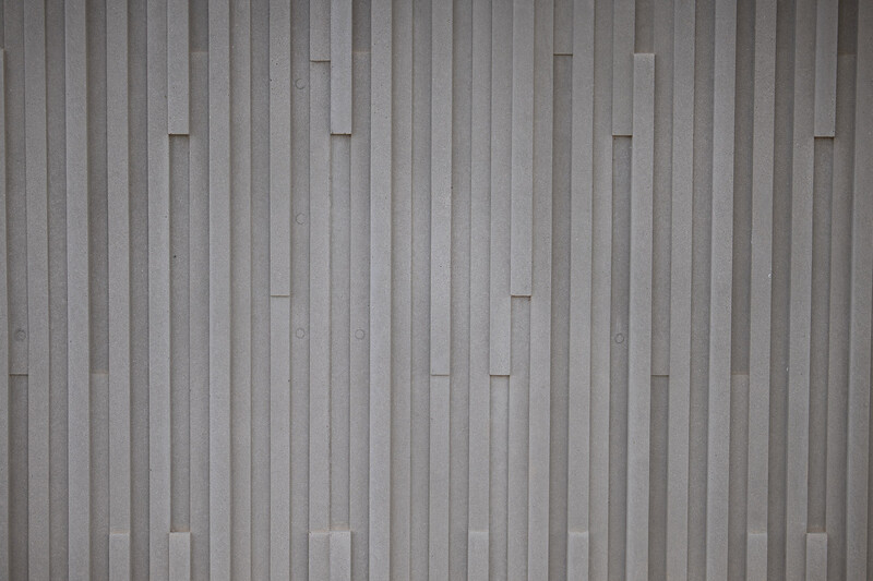 Corrugated metal wall with vertical ridges and regular horizontal seams creating uniform pattern.