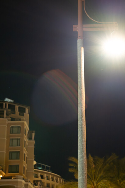 Tall street light illuminating a nighttime urban plaza with residential buildings and palm trees.
