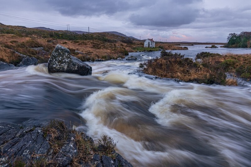 Long exposure of turbulent river with silky water flowing around dark rocks in moorland landscape.