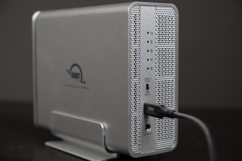 White external hard drive connected via USB cable to a silver desktop storage device with perforated metal casing.