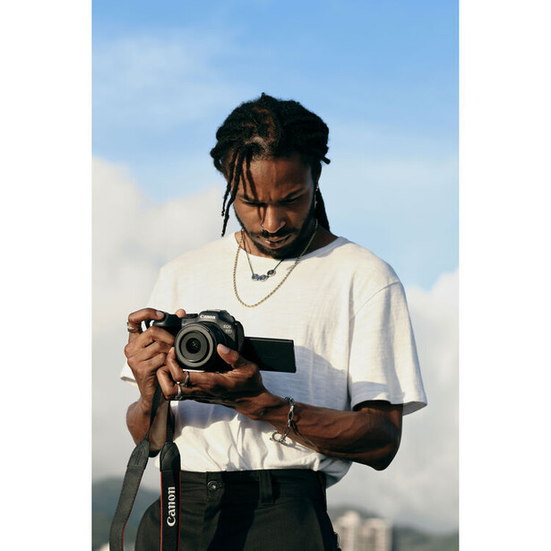 Photographer holding a professional video camera against a bright sky backdrop.