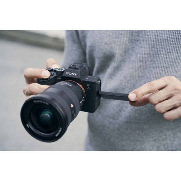 Photographer holding a Sony mirrorless camera with attached zoom lens in both hands.