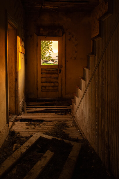 Long narrow corridor with warm golden light streaming through doorways at each end, creating strong directional shadows across the floor.
