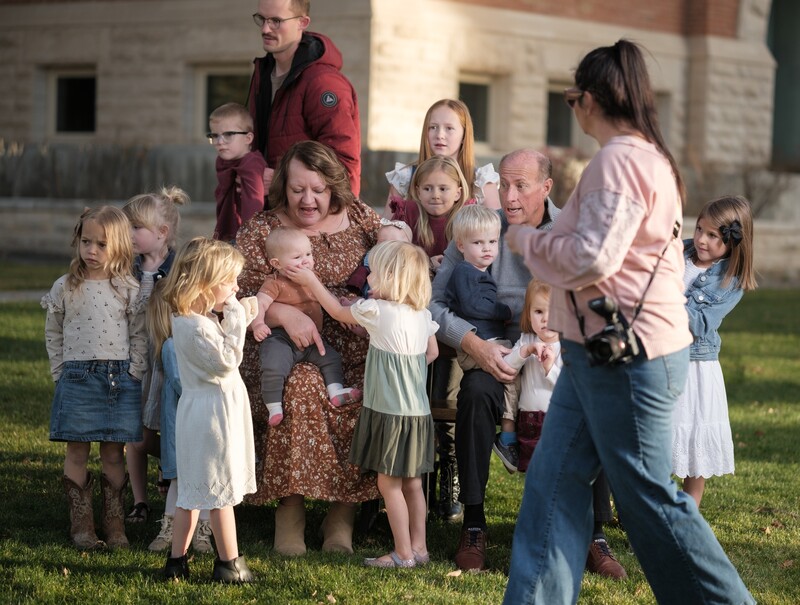 Multi-generational family group gathered outdoors on grass in front of a stone building.