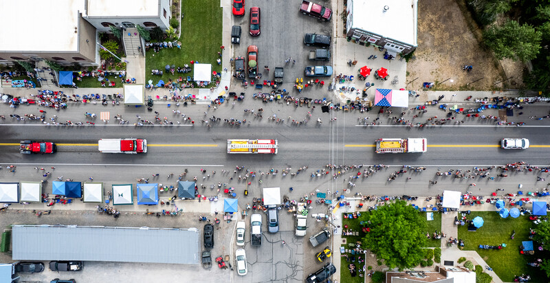 Aerial view of a parade route with marching bands, floats, and crowds lining both sides of a wide street.