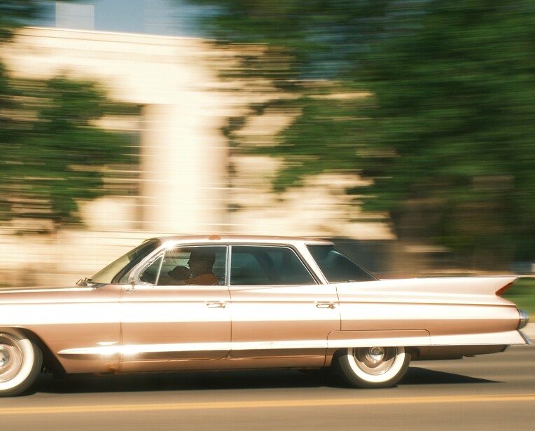 White vintage sedan in motion on a street with blurred background and trees.
