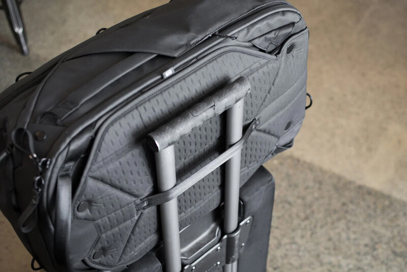Camera backpack with pass-through luggage handle attachment sitting on rolling suitcase.