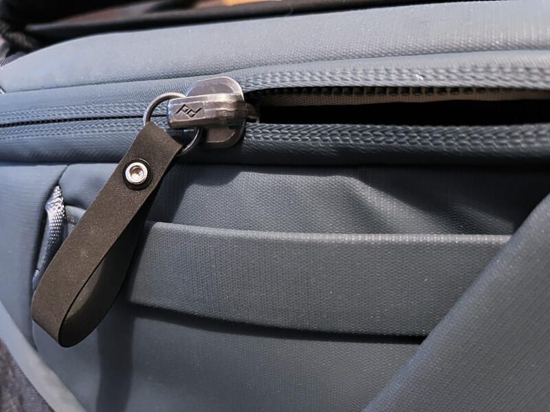 Close-up of a dark leather camera bag handle with metal hardware against gray fabric interior.