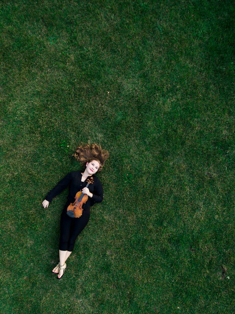 Musician lying on grass holding a violin, shot from directly above.
