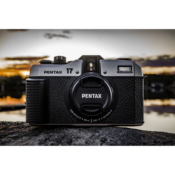 Pentax 17 film camera positioned on a rocky surface with a blurred golden-hour landscape in the background.