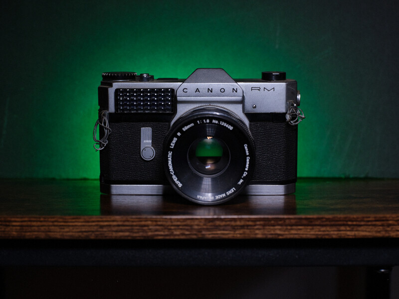 Canon 7 rangefinder camera with 50mm lens on wooden surface against green backdrop.