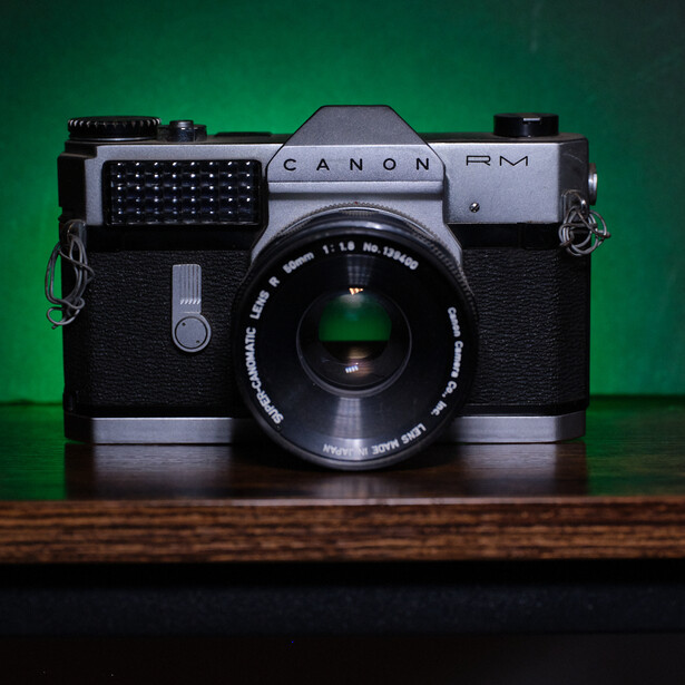 Canon FM rangefinder camera with black leather body and chrome top plate on wooden surface against green backdrop.