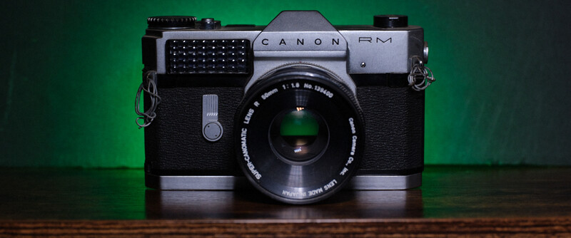 Canon RM rangefinder camera with black body and chrome top plate against green background.