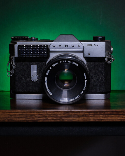 Canon FK rangefinder camera with black body and chrome top plate against green background.
