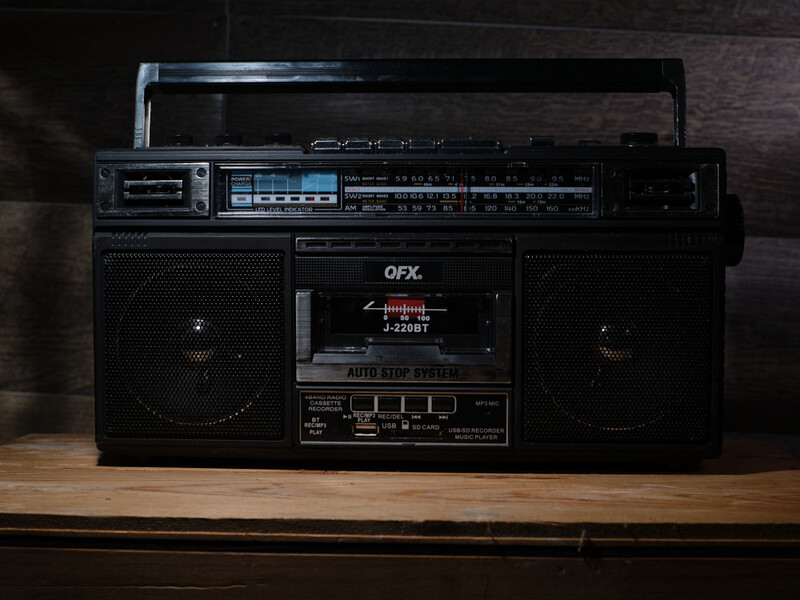 Black vintage boombox with dual cassette decks and AM/FM radio tuner on wooden surface.