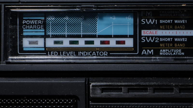 Close-up of a vintage radio's display panel showing LED level indicator, frequency bands, and power/charge controls.