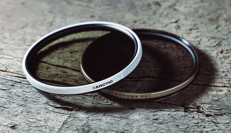 Two camera lens filters stacked on weathered wood surface, one white-rimmed and one dark-rimmed with visible text markings.