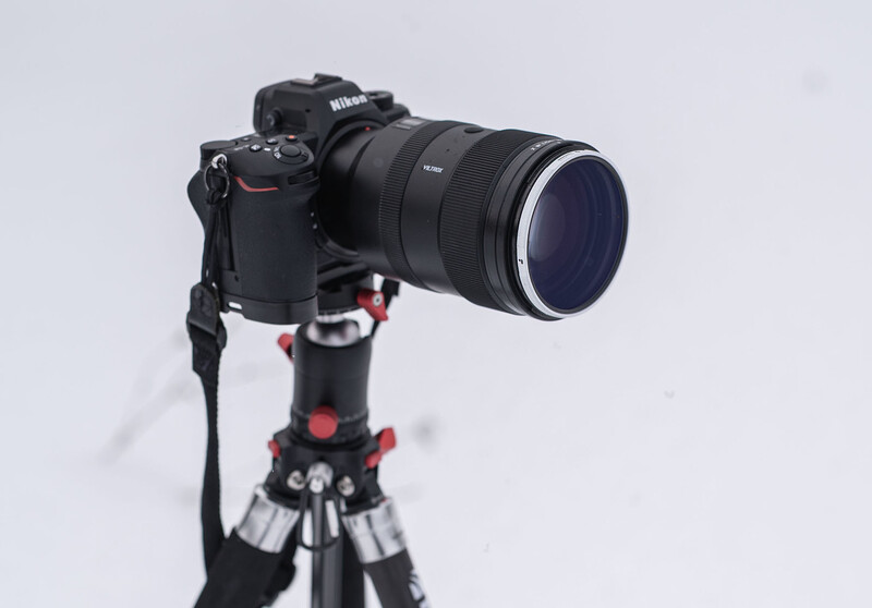 Nikon DSLR camera with telephoto lens mounted on a tripod with red ball head.