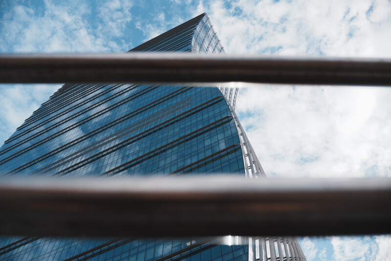 Modern glass skyscraper shot from below with horizontal steel beams framing the composition against a blue sky.