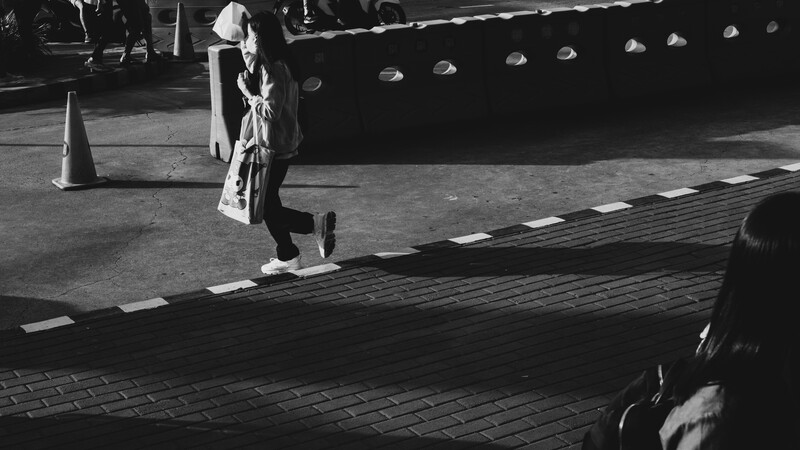 Woman crossing a striped crosswalk in front of a large truck in black and white.