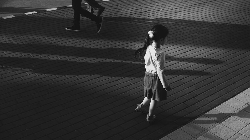 Woman walking across a brick plaza in sunlight, casting a long shadow in black and white.