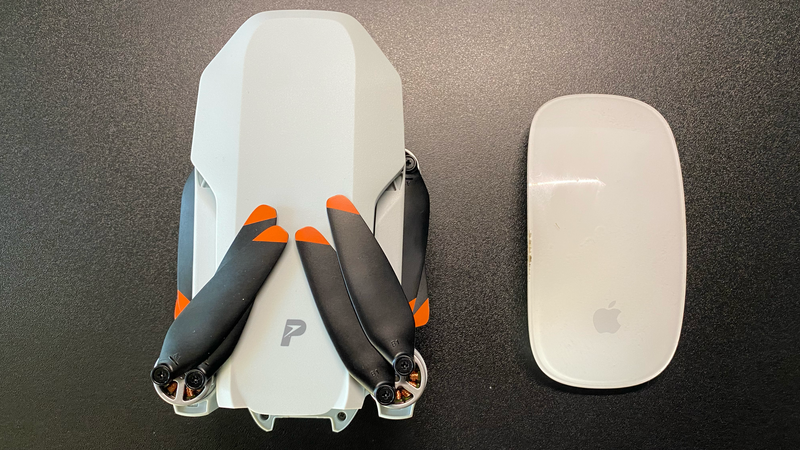 Overhead view of a white drone with black arms and orange accents next to a white computer mouse on dark surface.