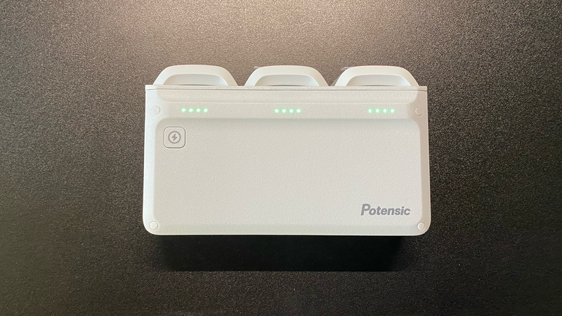 Potensic portable battery charging station with three cylindrical battery slots and LED charge indicators on dark surface.