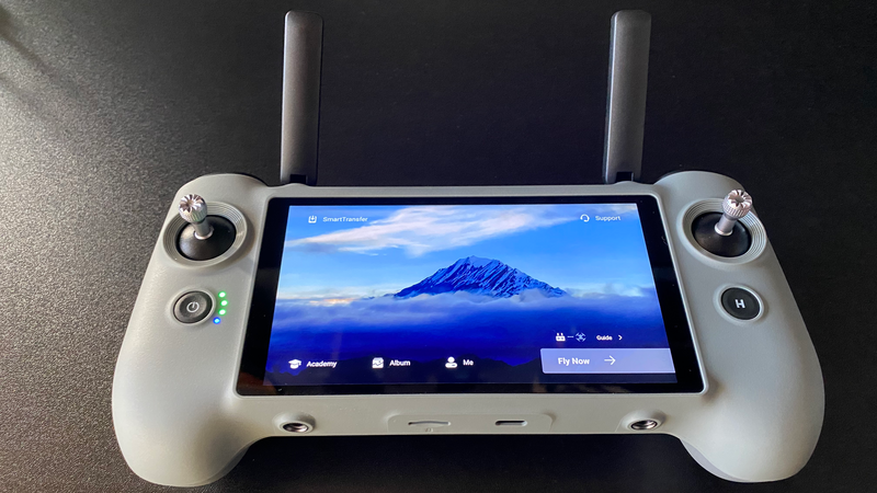 Drone remote controller with integrated display screen showing aerial footage of a snow-capped mountain.