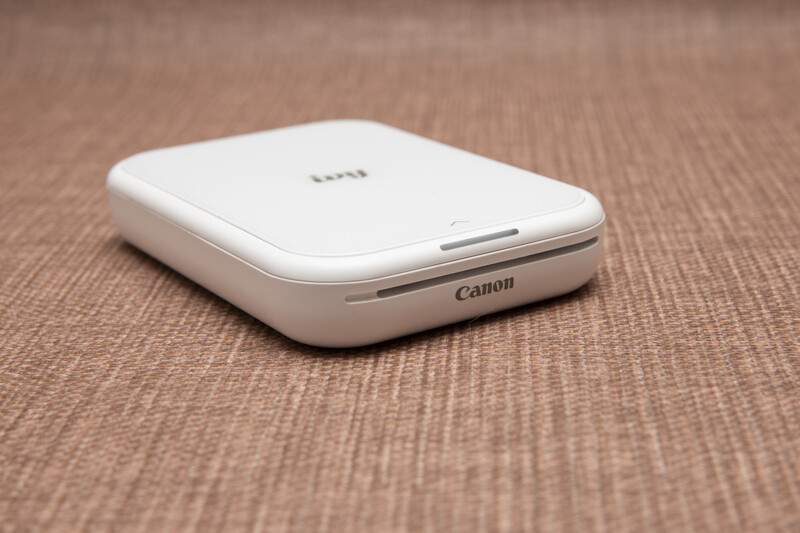 Canon Zoemini portable photo printer in white, displayed on a textured beige fabric surface.