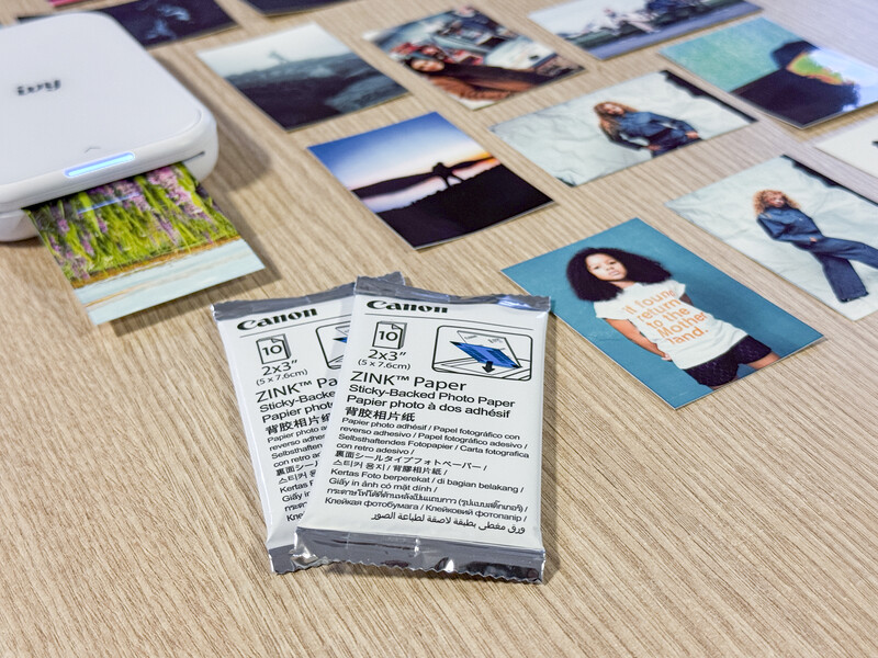 Canon Zink paper package surrounded by printed photographs on a wooden surface.