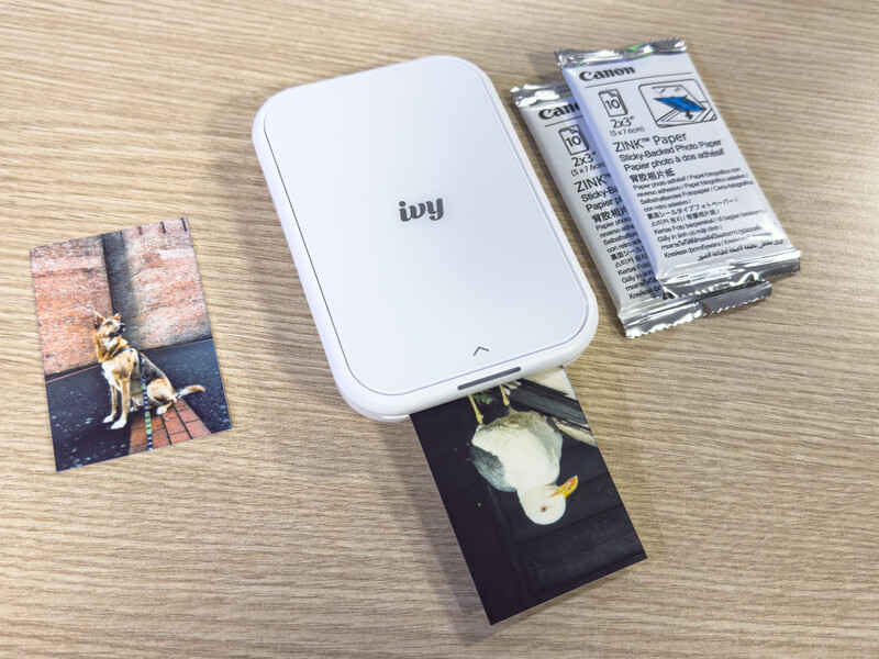 Ivy portable photo printer with printed photos and instruction manuals displayed on wooden surface.