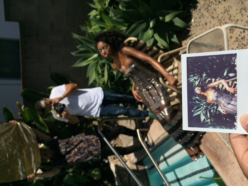 Photographer holding a Polaroid instant photo while shooting in a tropical garden setting.