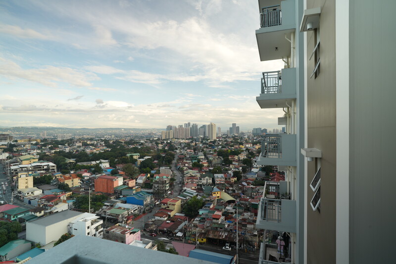 View from a high-rise balcony overlooking a dense urban cityscape with residential neighborhoods and distant downtown buildings.