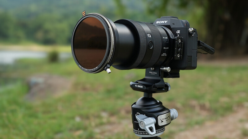 Sony mirrorless camera with telephoto lens and neutral density filter mounted on tripod head outdoors.