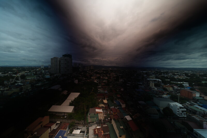Aerial view of a city under dramatic storm clouds with dark sky and bright center light break.