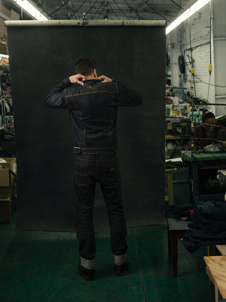Person standing with hands behind head against large black backdrop in workshop studio.